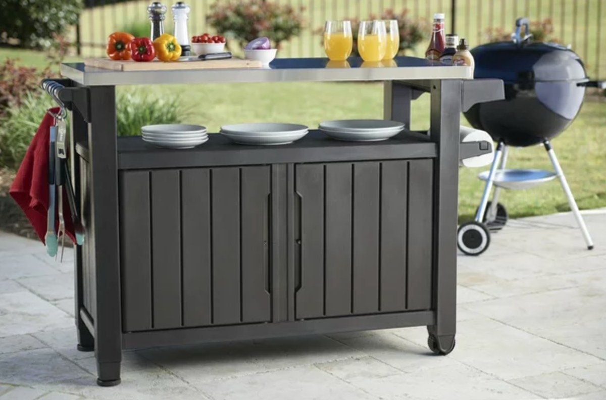 the dark buffet table with a metal top with ingredients and dishware in front of a grill
