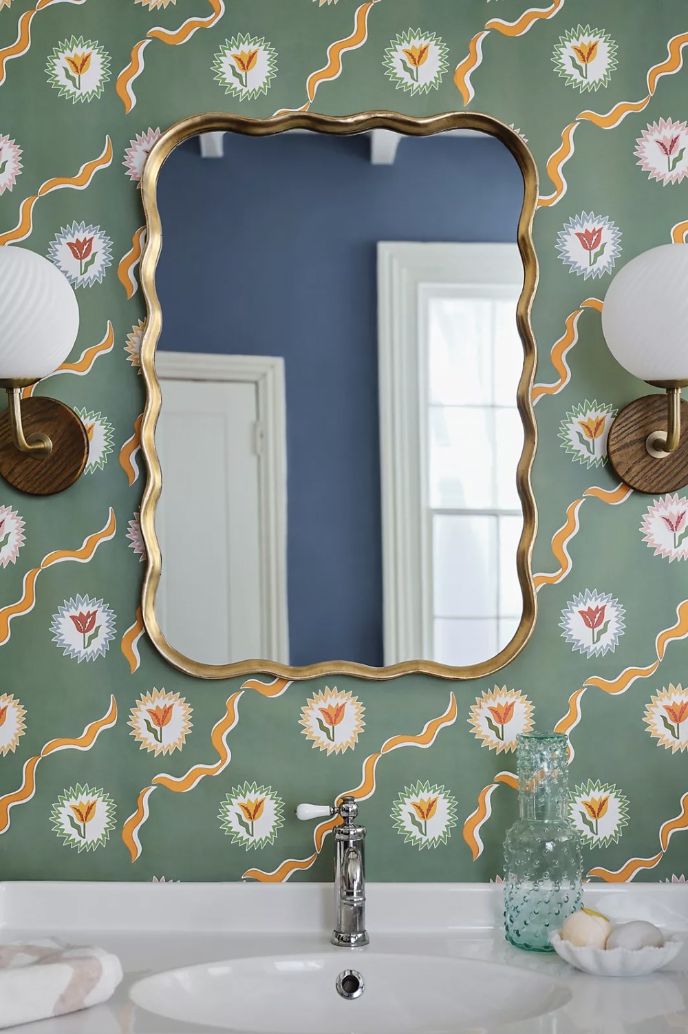 The wall mirror hanging above sink on patterned wallpaper