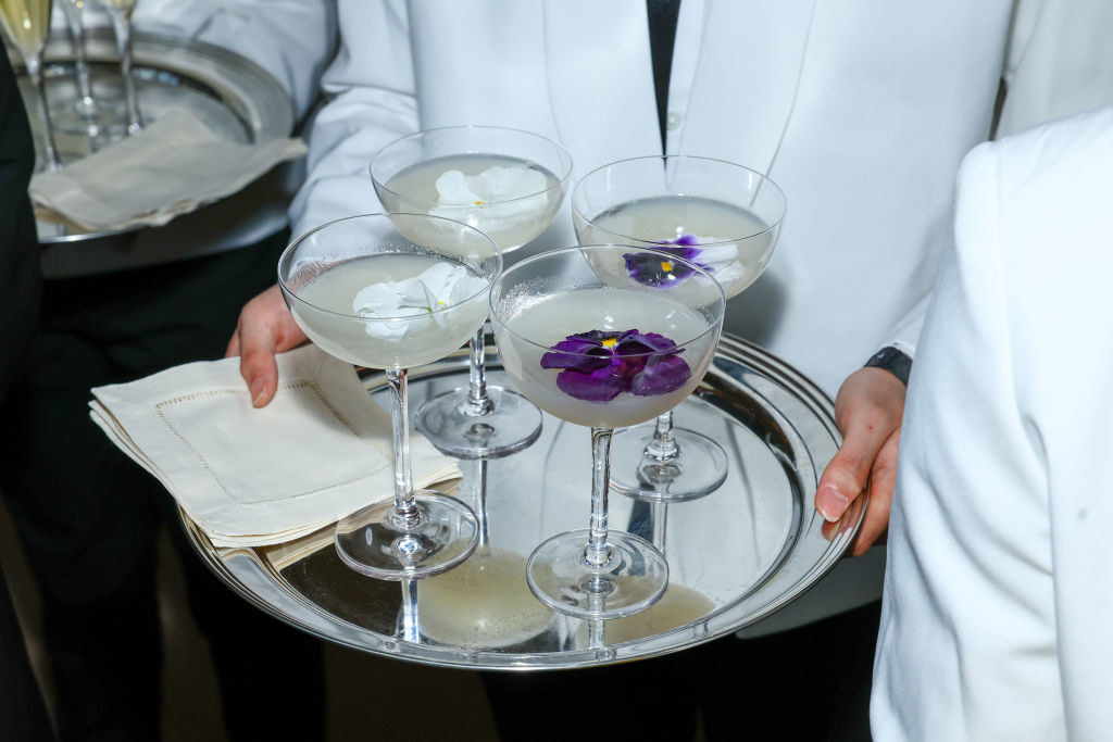 A tray of white cocktails with flowers inside the drink