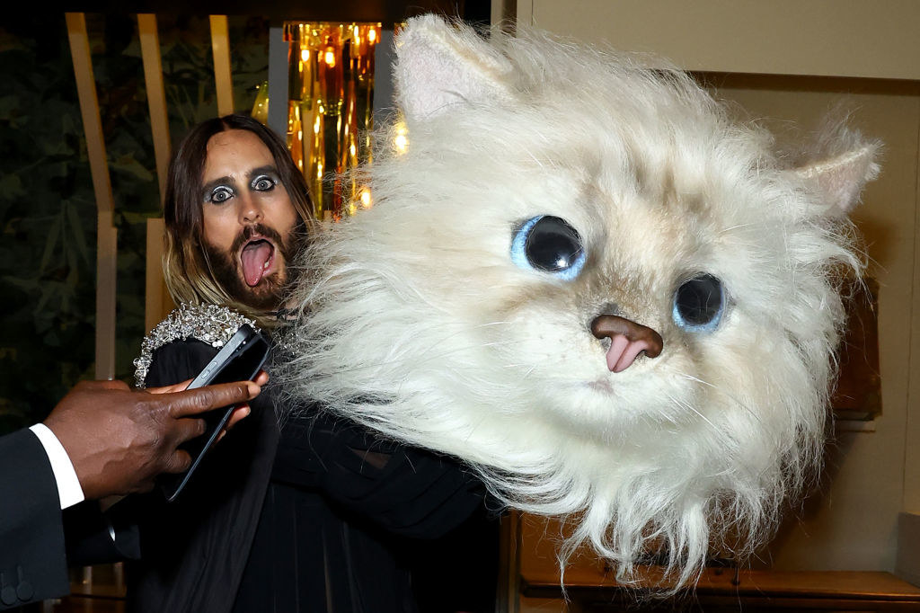 Jared Leto sticks his tongue out while holding a mascot-sized cat head