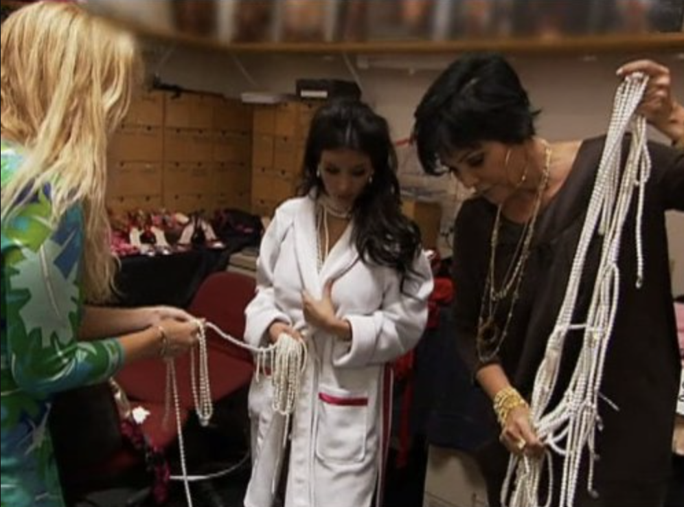 Kris Jenner holding long pearl necklaces as Kim looks on before the photoshoot