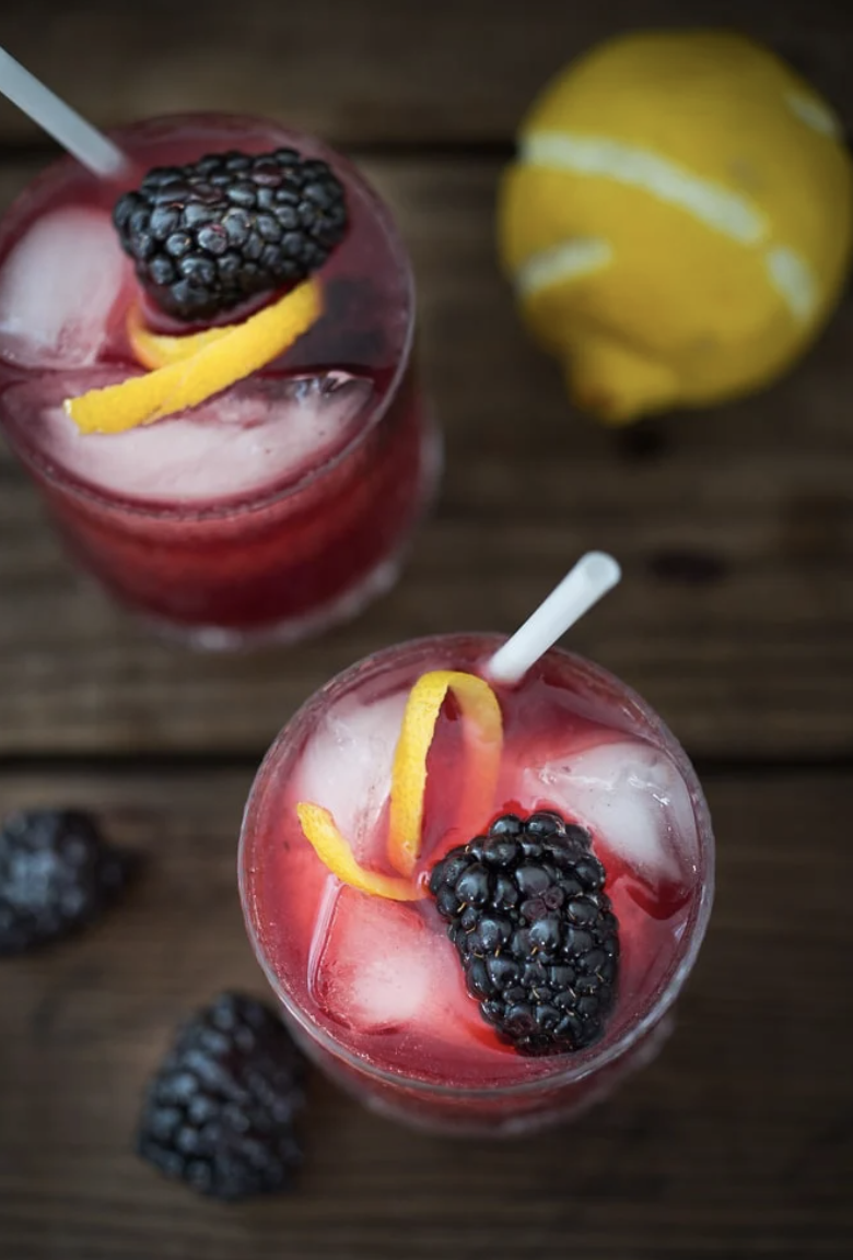 Two blackberry cocktails with lemon wedge garnish.