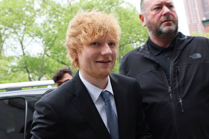 Closeup of Ed Sheeran walking into a courtroom while wearing a suit and tie