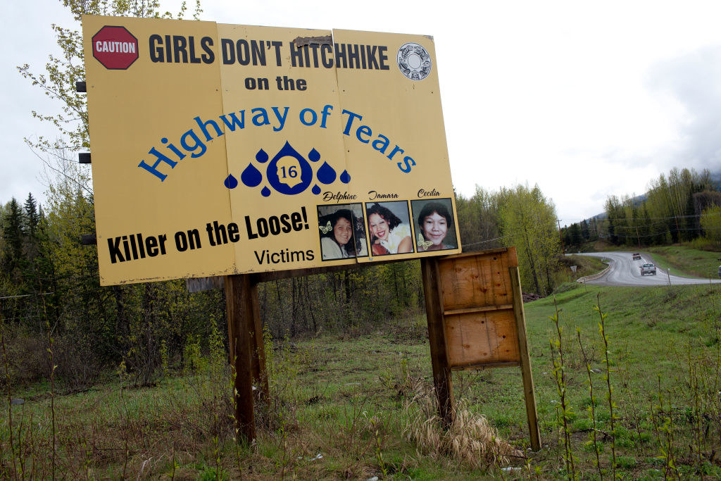 Cars drive past a road sign on Canada&#x27;s Route 16 that says girls don&#x27;t hitchihike on the highway of tears, killer on the loose