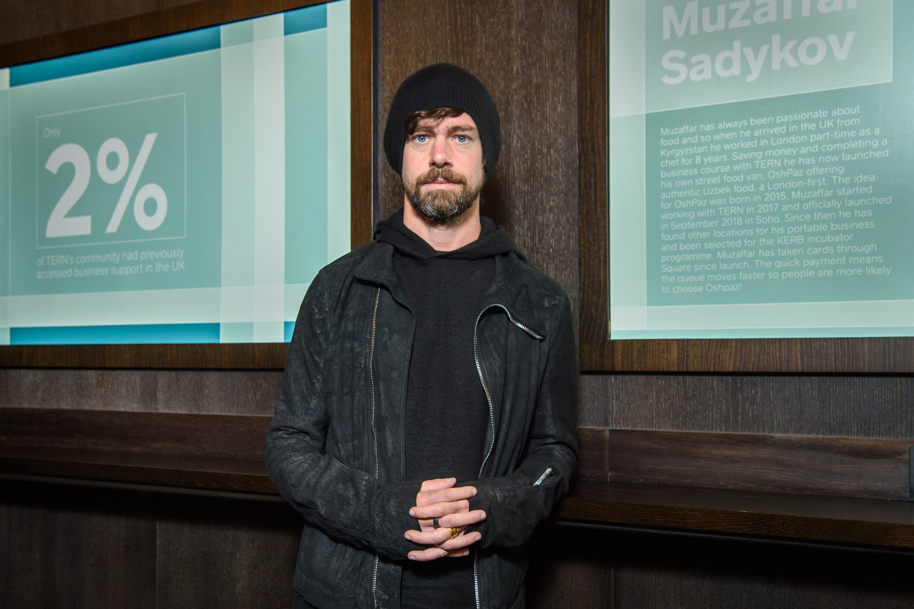 Jack Dorsey, standing in front of a screen, wearing all black and a black beanie
