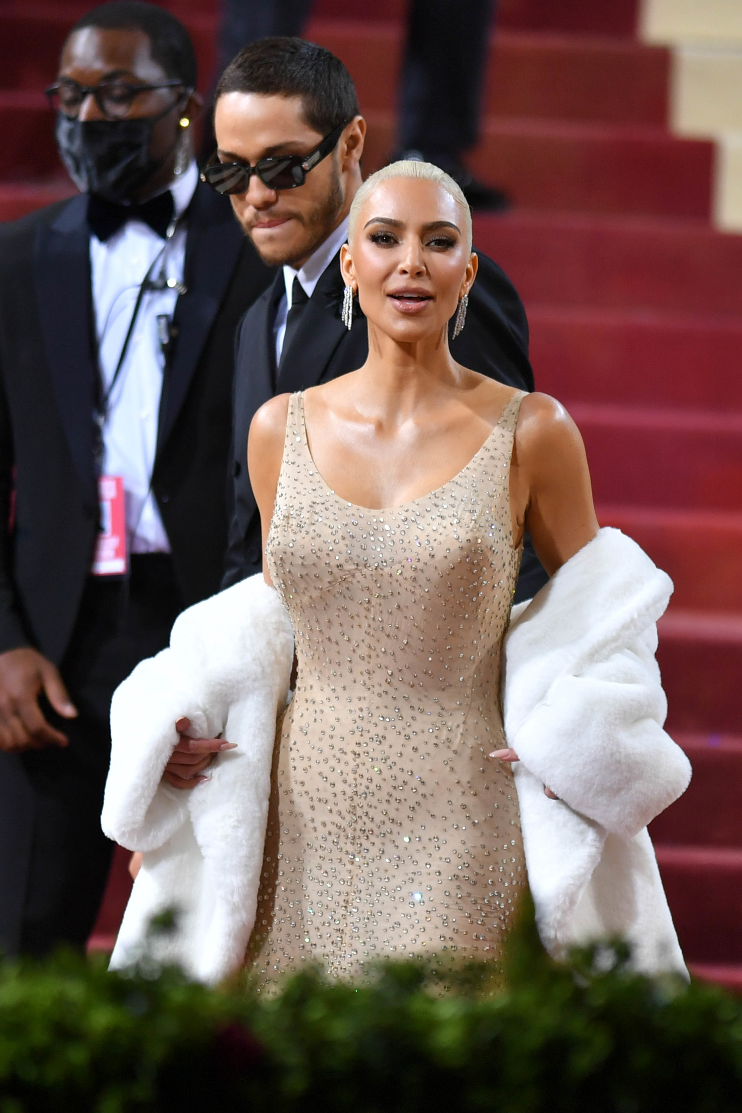 Kim Kardashian on the red carpet wearing a tight beige sequinned dress and a fluffy white coat around her arms