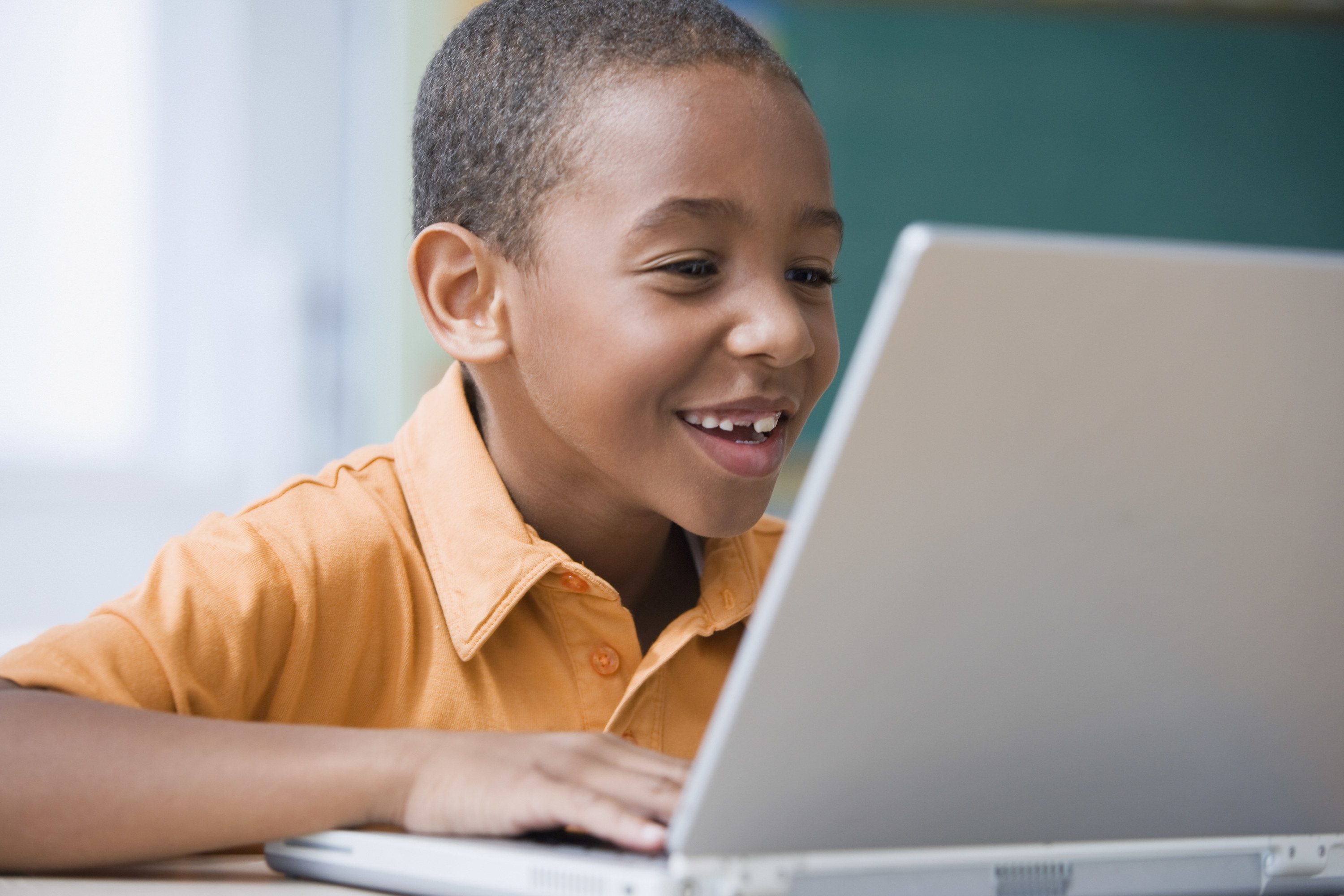 A kid smiles while playing on a laptop