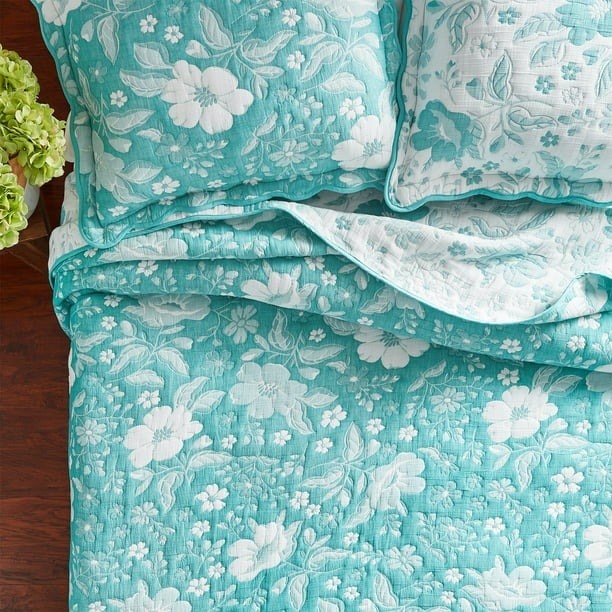 the aqua and white floral quilt on a bed