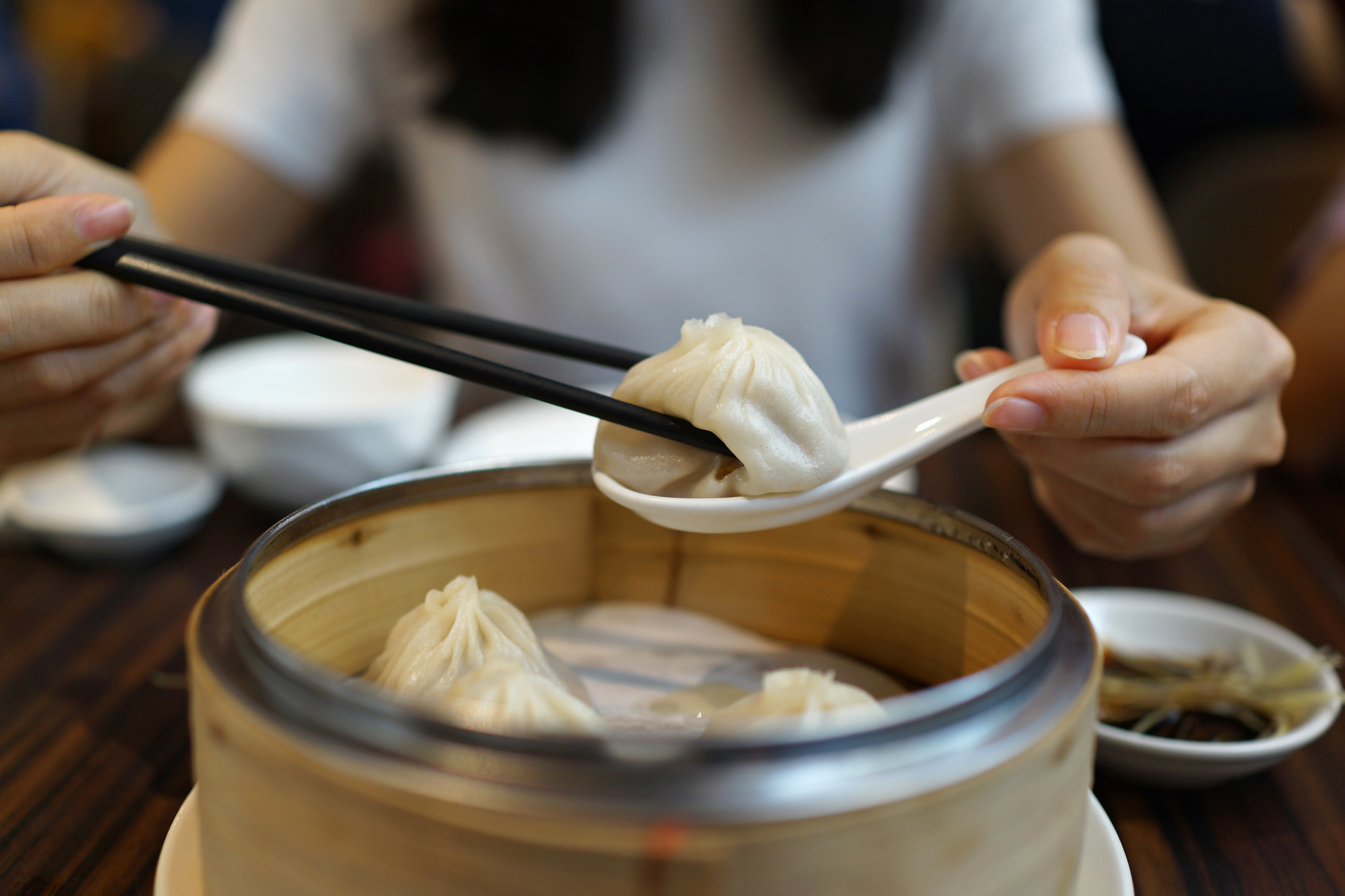 Dumplings in a tan bamboo bowl woman holding white spoon and black chopsticks