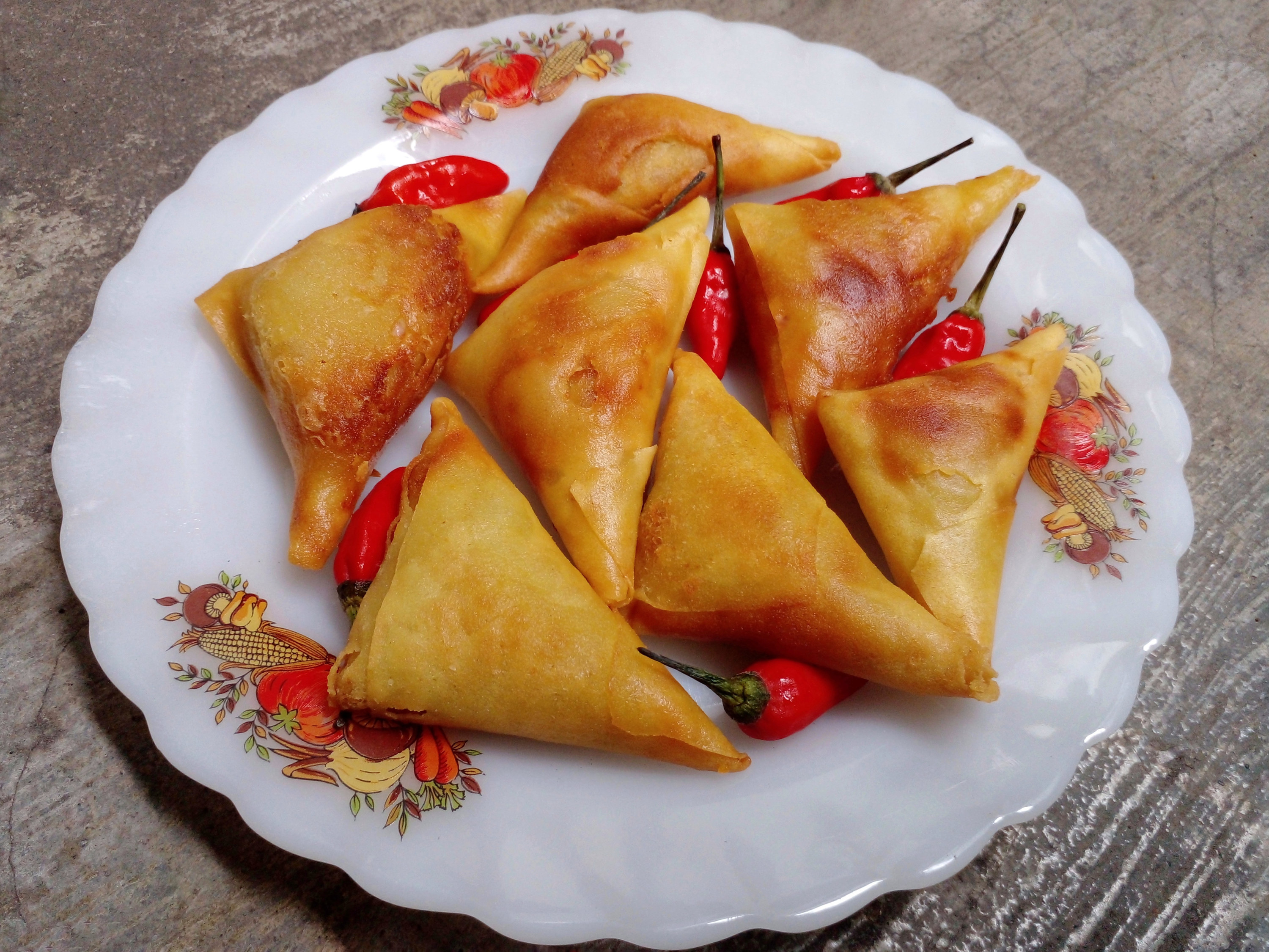 A white plate filled with seven fried samosas and red chilis