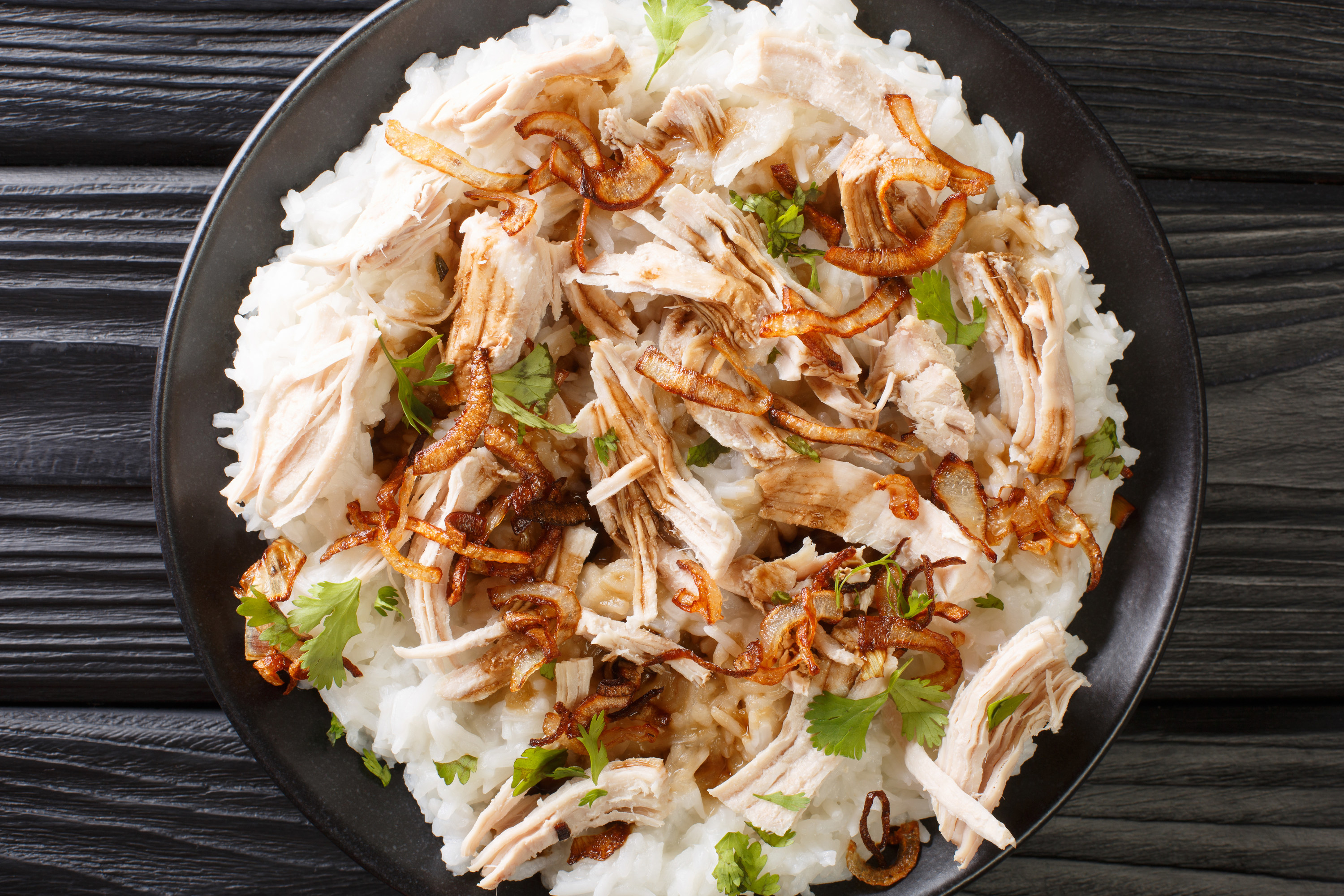 shredded turkey over white rice on black plate on top of black wood table