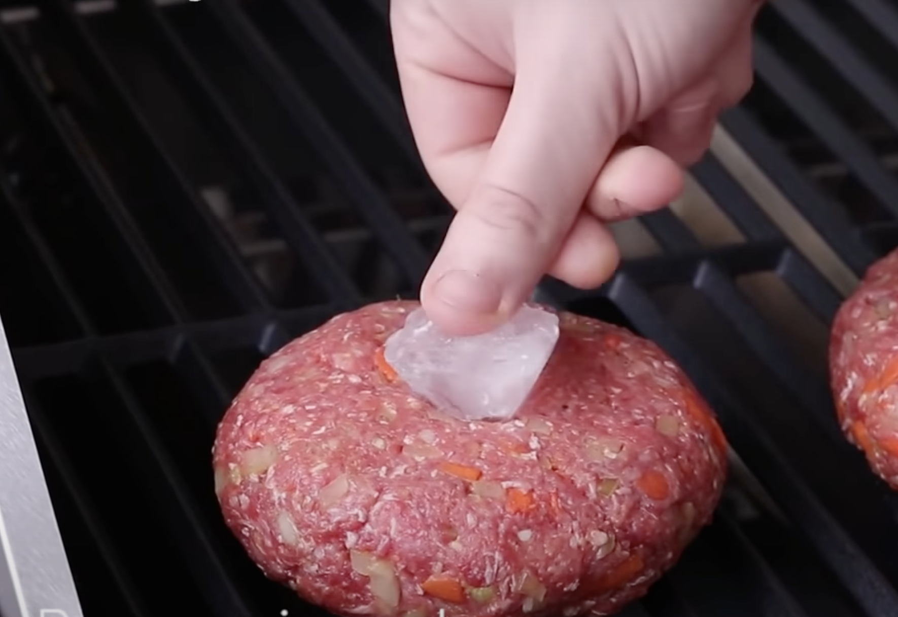 A hand pressing an ice cube into a burger patty.