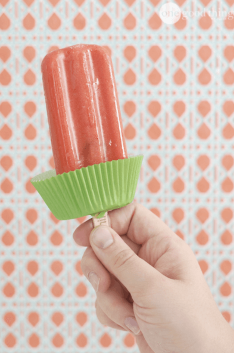A person holding a ice pop with a cupcake liner.