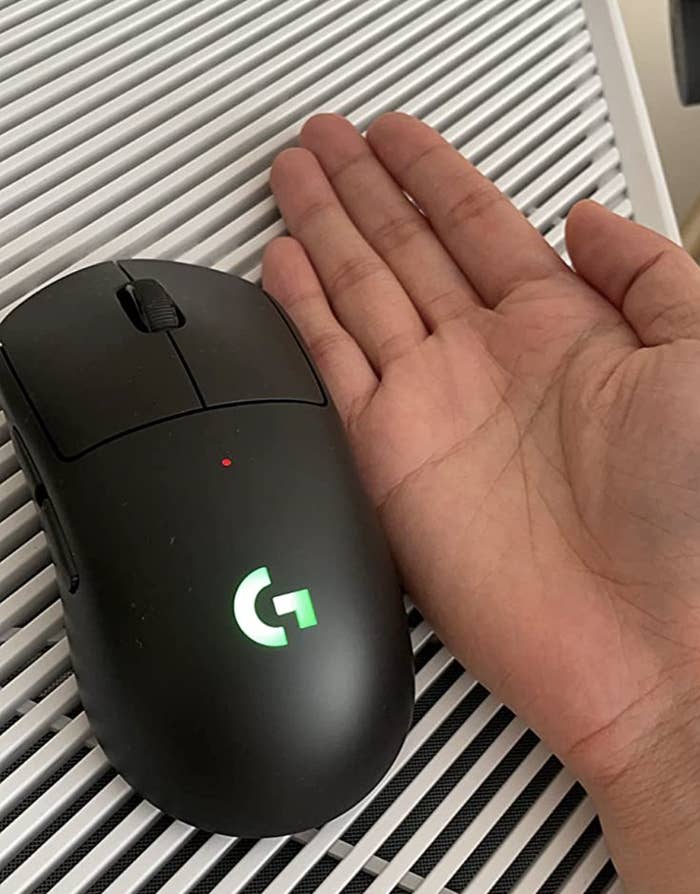 reviewer putting their hand next to the slightly smaller mouse for size reference