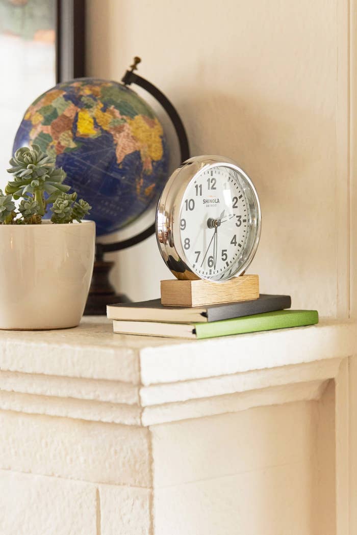 a silver round desk clock on a wooden stand