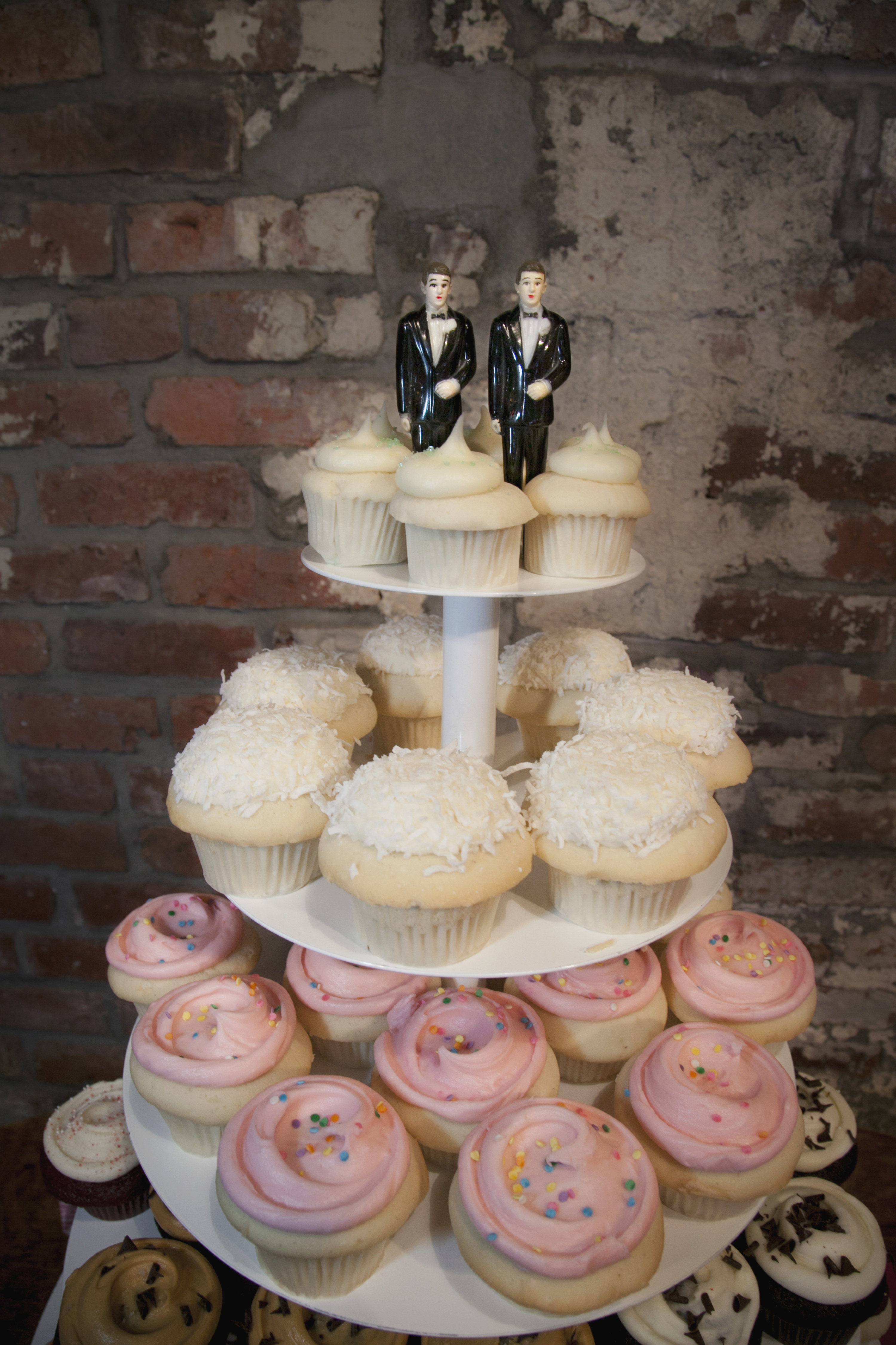 Two male figurines sit on top of a cupcake dessert display at a wedding