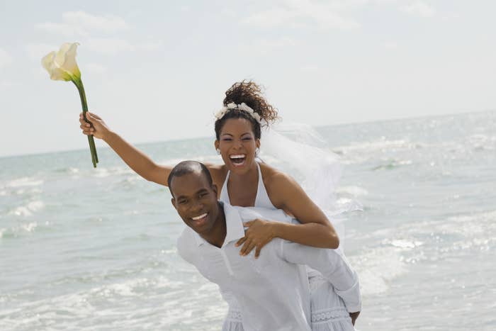 A groom gives a bride a piggyback ride as they're pictured by the water