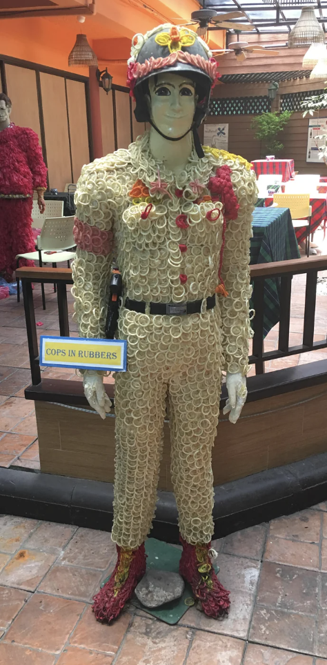 A cop mannequin with a head-to-toe condom outfit, including shoes and a helmet embellished with condoms, with a &quot;Cops in Rubbers&quot; sign