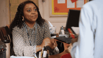 teacher looking confused and shrugging at her desk