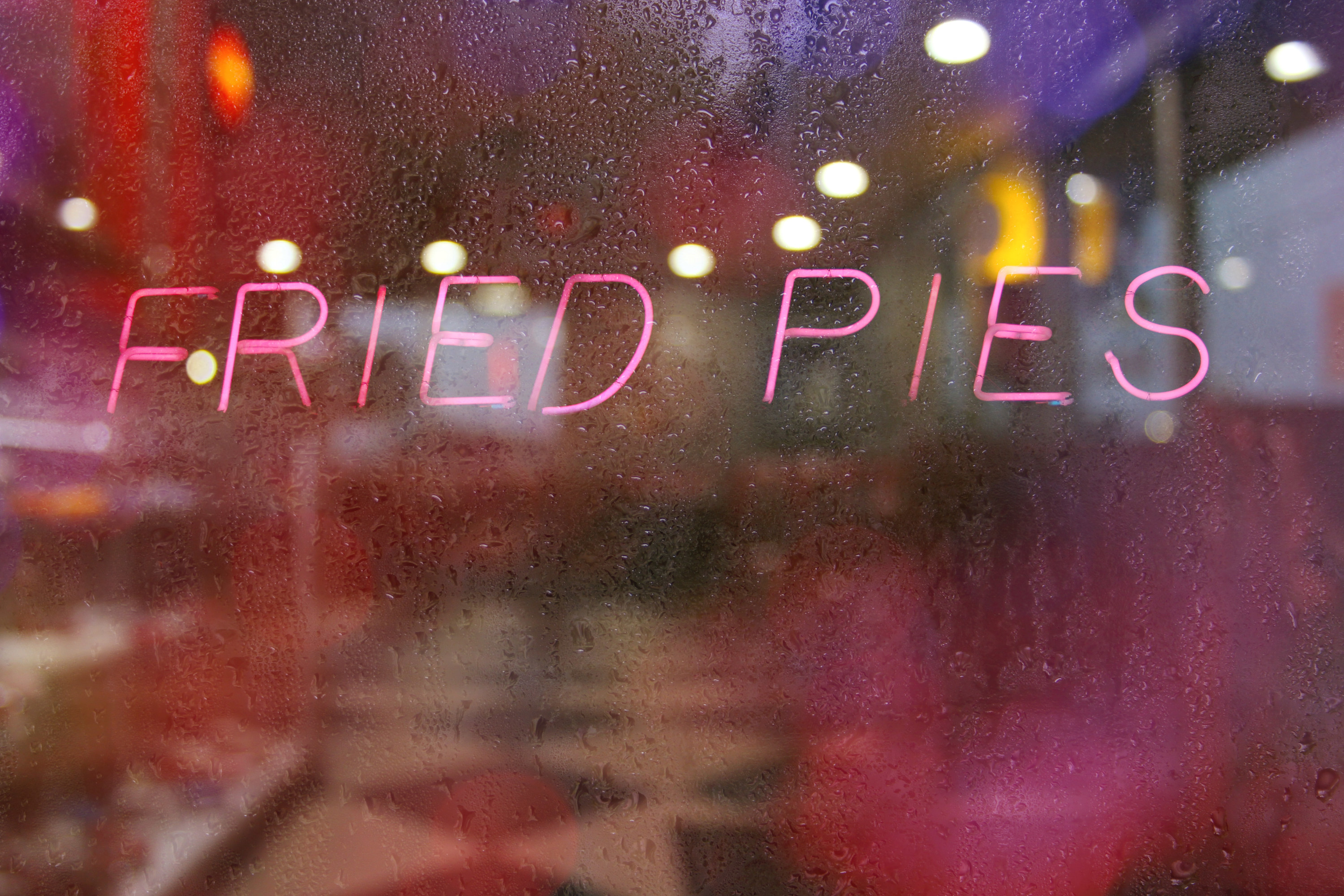 a pink neon sign spelling fried pies on a rainy window background in a diner