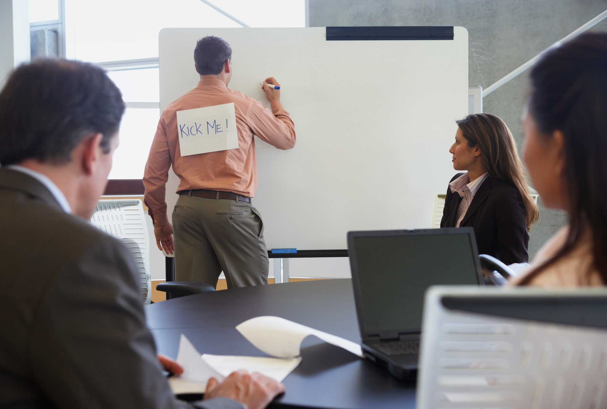Man at office with a &quot;KICK ME!&quot; sign on his back