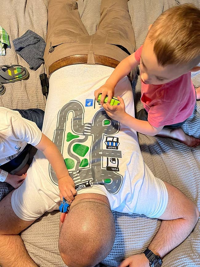 a reviewer laying on the couch with his two children playing cars on a racetrack shirt on his back