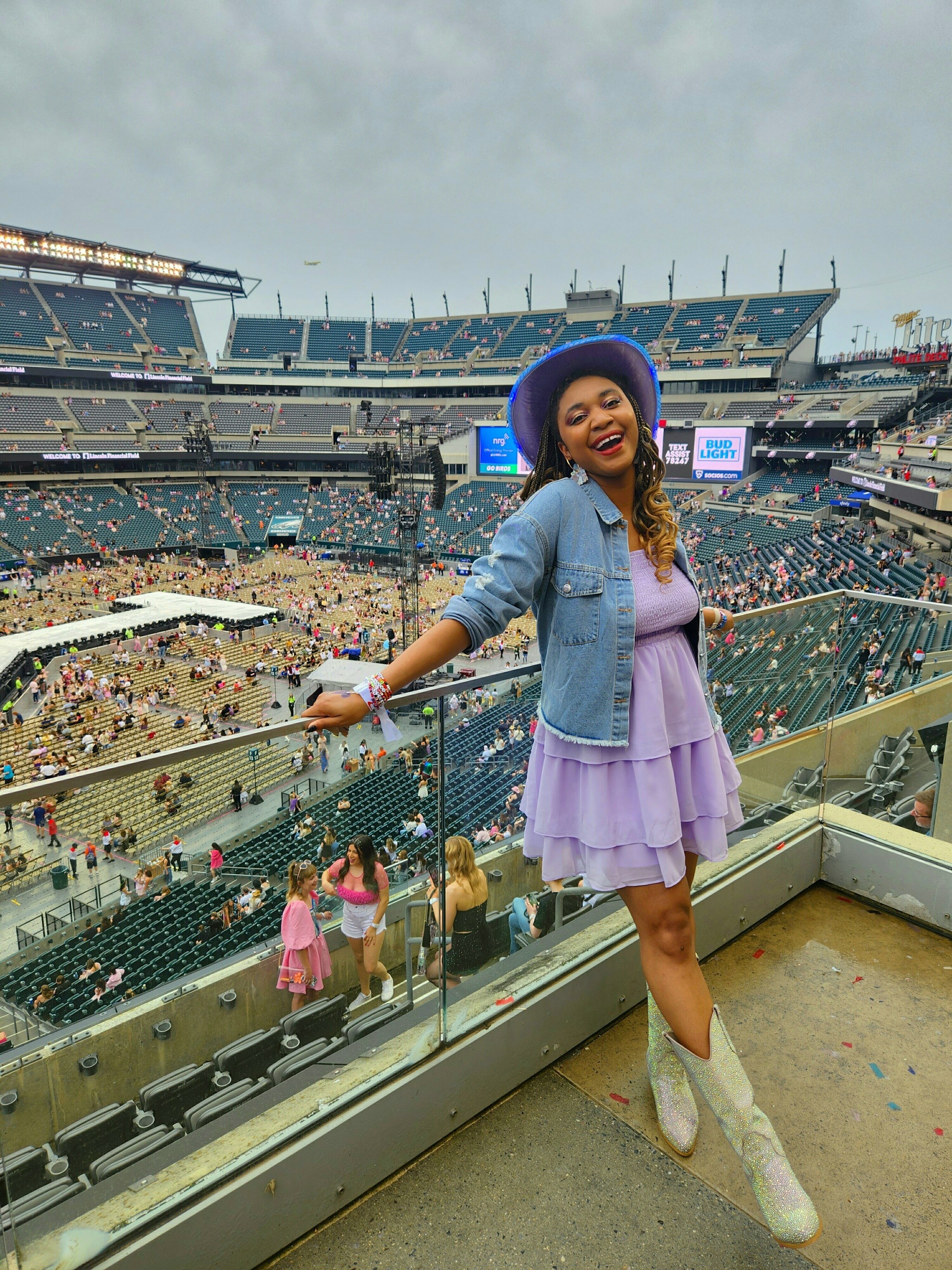 woman wearing a denim jacket over a ruffled dress with cowboy boots and hat