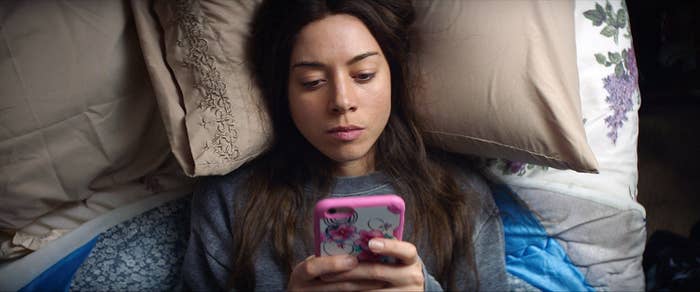 Ingrid laying in bed and looking at her phone in a scene from &quot;Ingrid Goes West&quot;