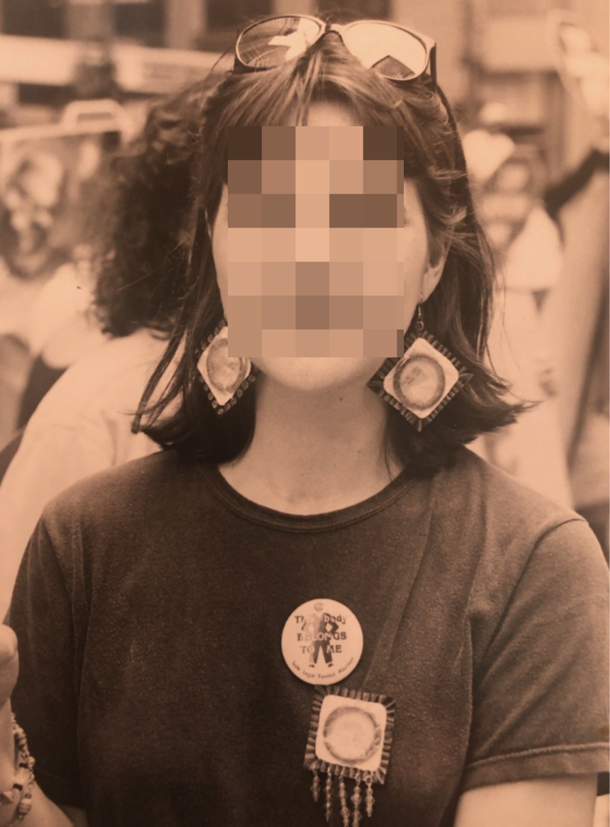 Woman with pixelated face showing condom earrings and pin