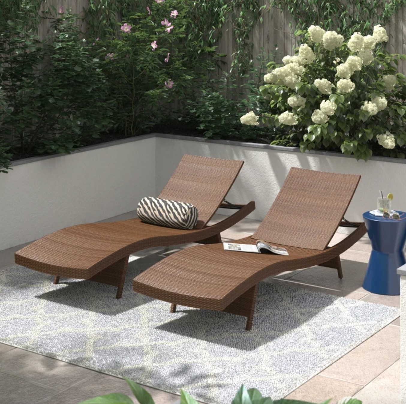 the two dark brown wicker chaises on a patio with cushions and blankets