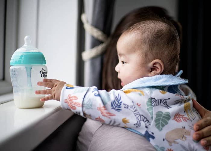 infant being held on sofa while reaching for bottle on windowsill