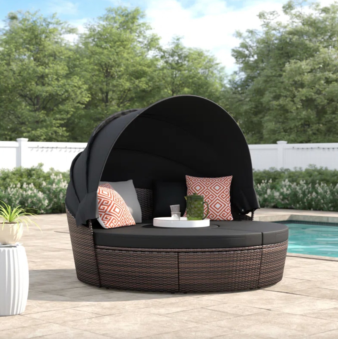 the dark wicker and dark brown cushioned daybed with a dark brown cover and decorative pillows, on a pool deck