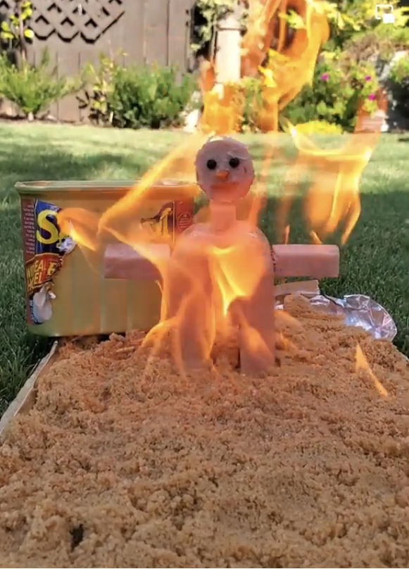 A &quot;Burning Man&quot;-type figure on fire above a sheet of Spam lying on the grass