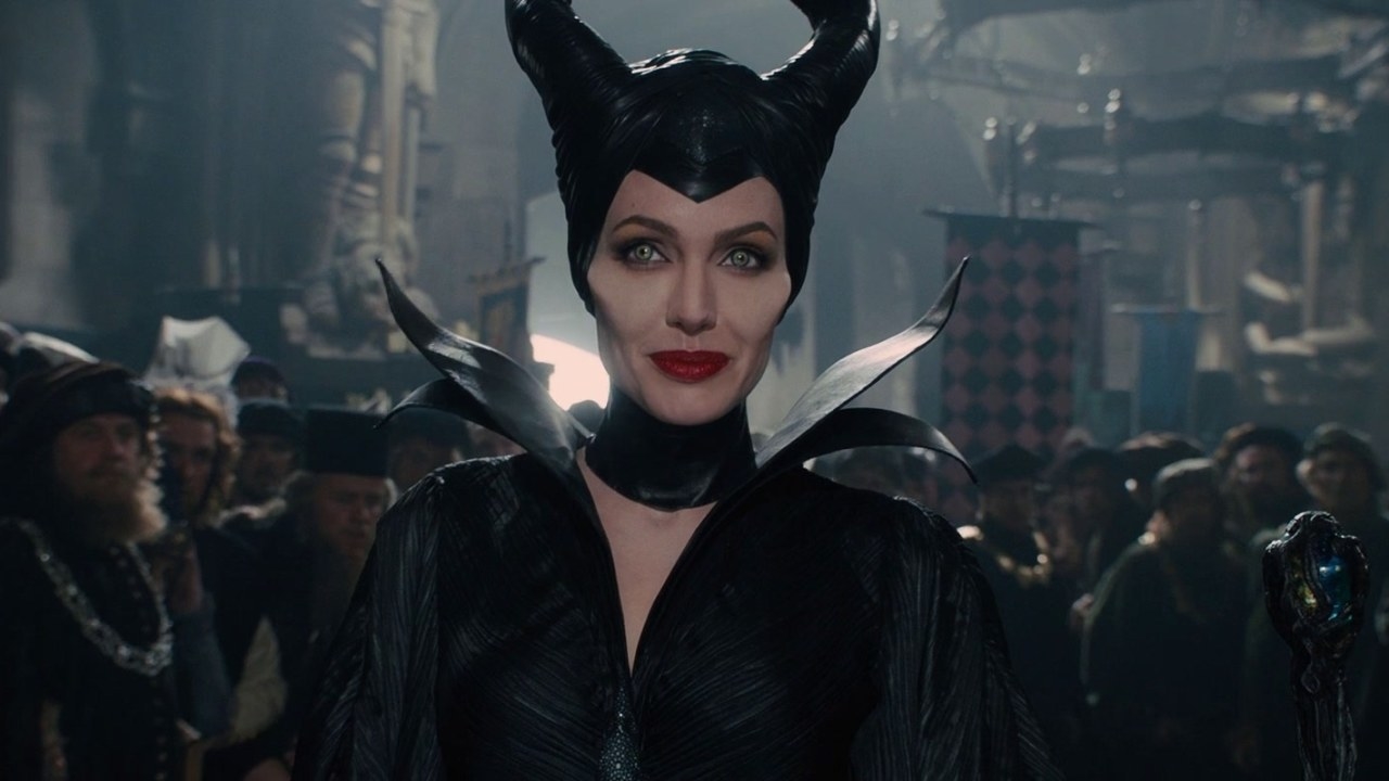Maleficent with horns and staff, black attire, standing amidst a crowd