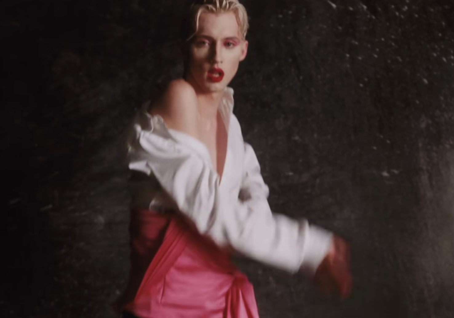 In a screenshot from Troye Sivan&#x27;s music video Bloom, he&#x27;s wearing an off-the-shoulder white shirt and pink wrap pants