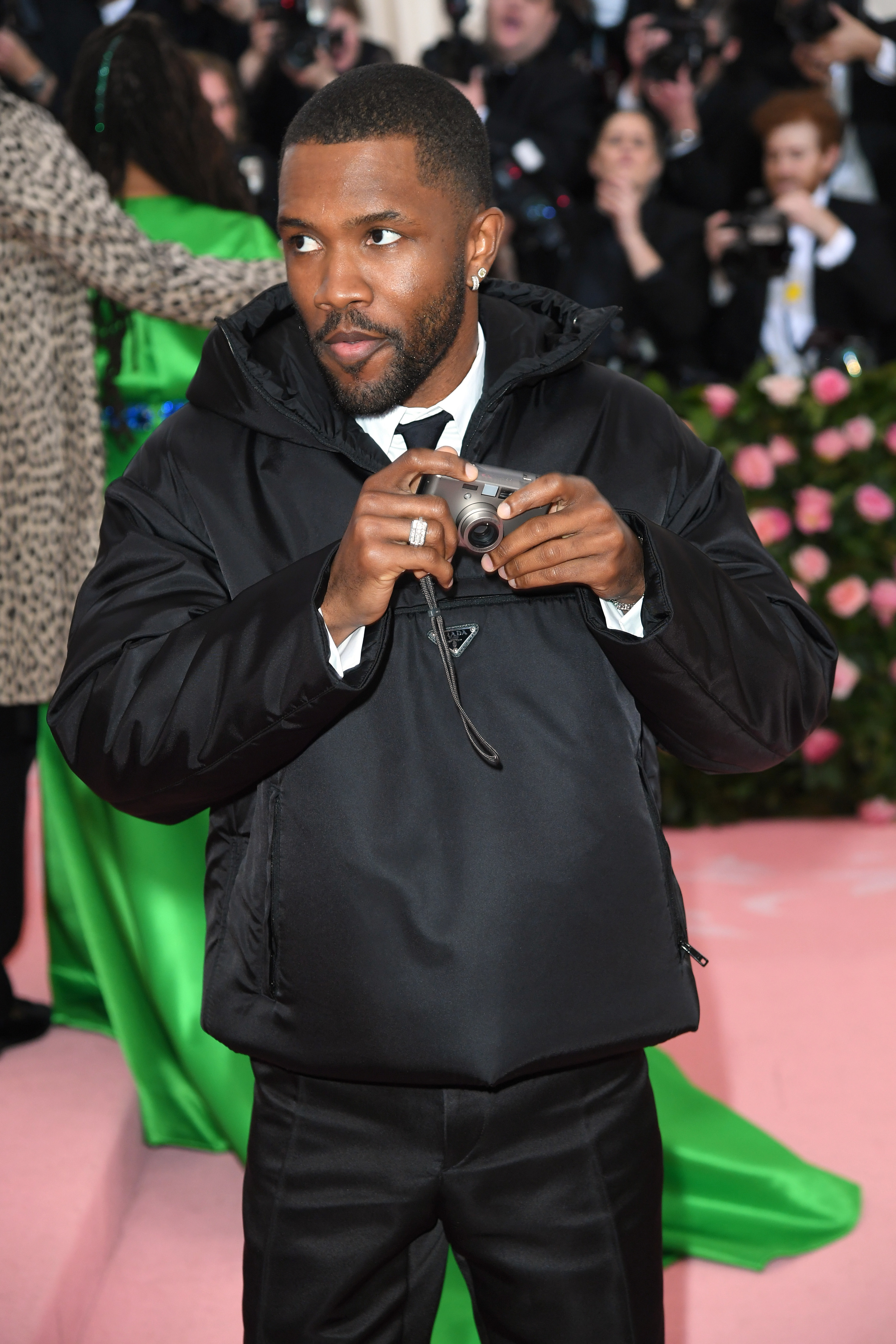 Frank Ocean on the Met Gala red carpet, wearing a black suit and Prada jacket and holding a film camera