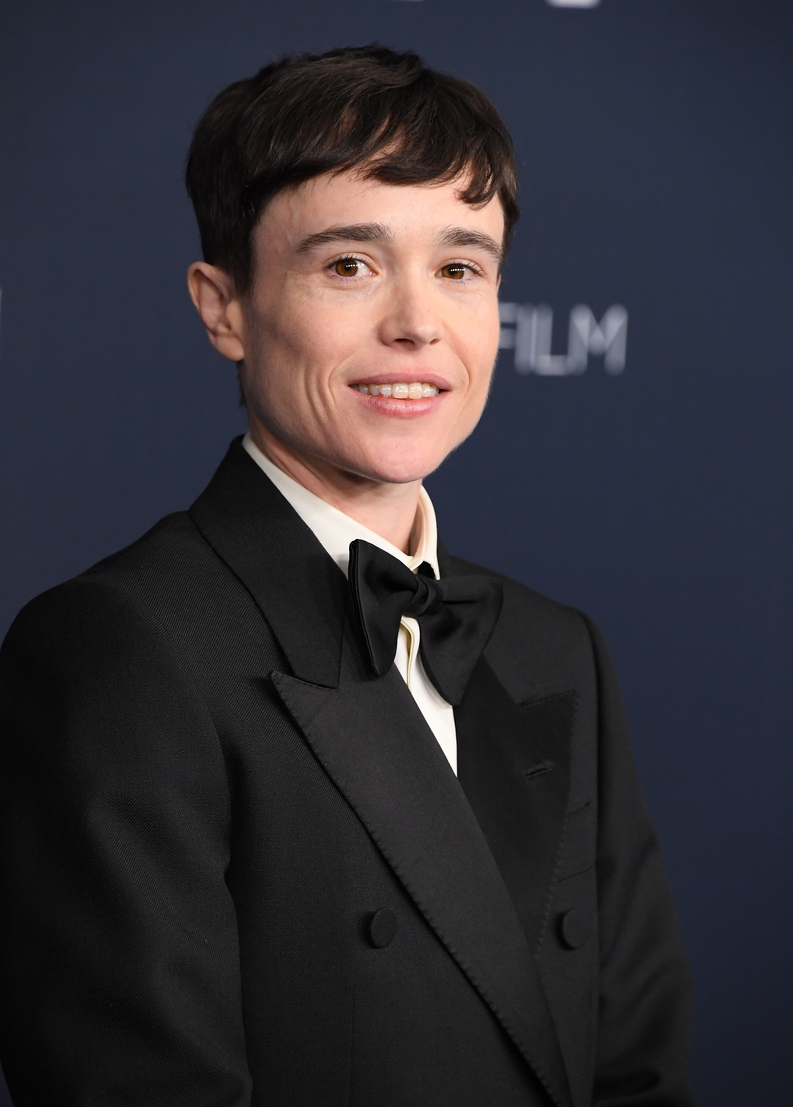 Elliot Page smiling on a red carpet wearing a black tux