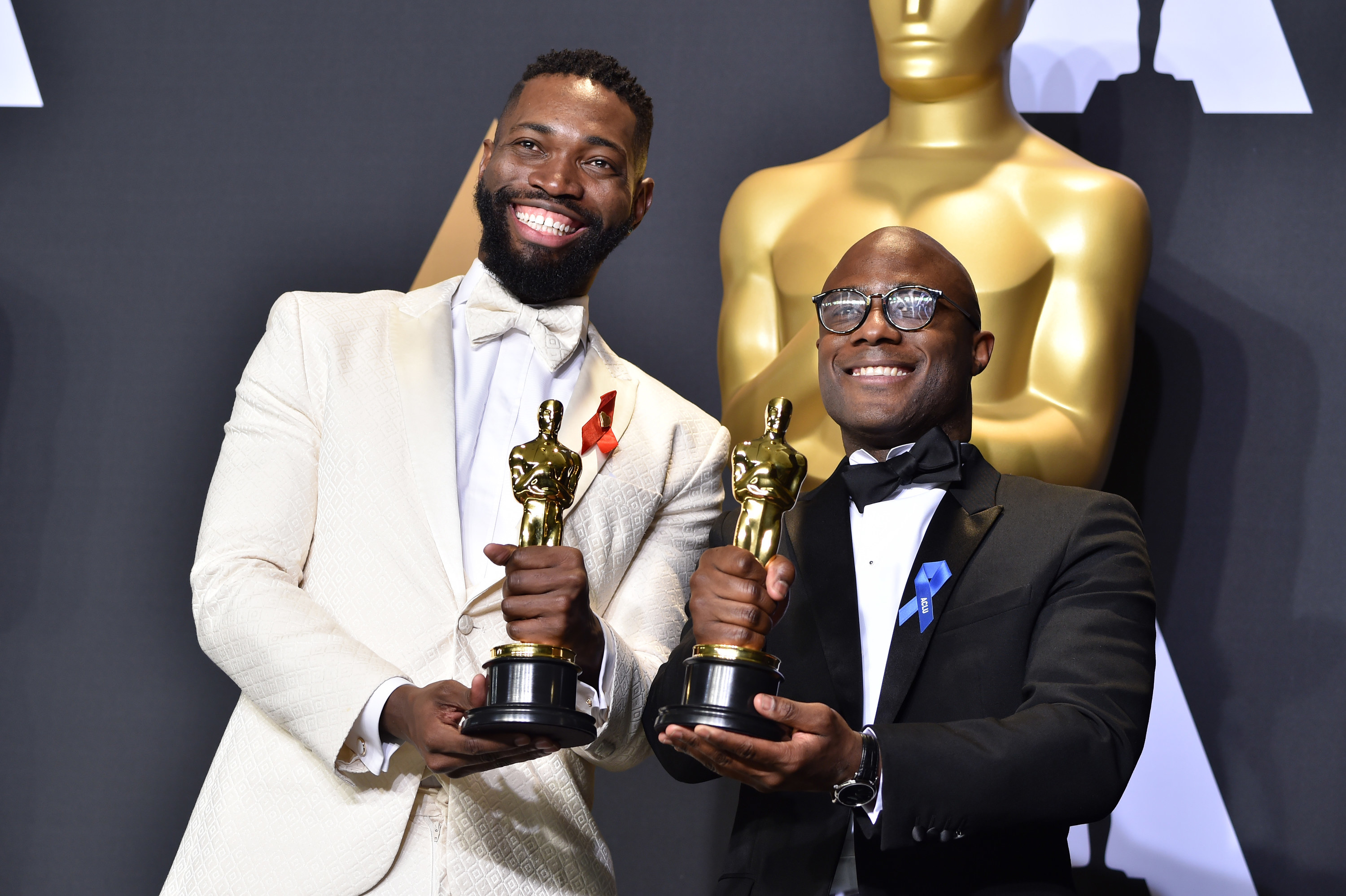 Barry Jenkins and Tarell Alvin McCraney holding Oscars, smiling. and posing in suits