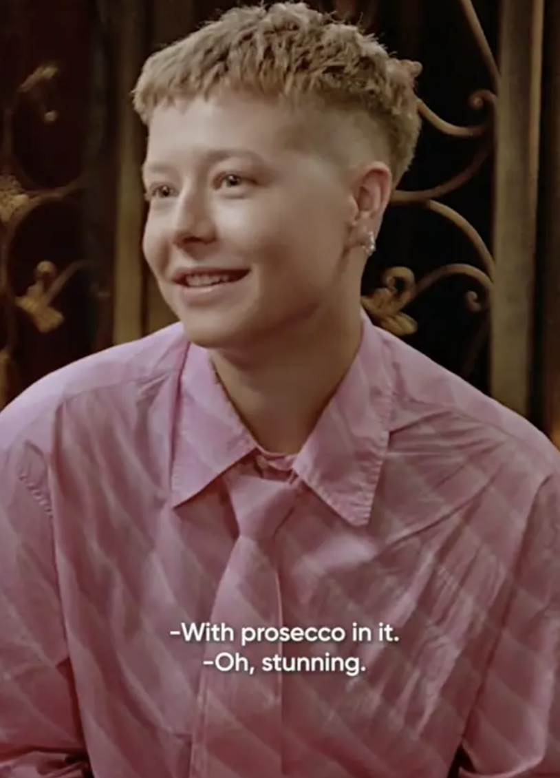 A screenshot of Emma D&#x27;Arcy in a pink striped shirt and matching tie, with a caption saying &quot;With prosecco in it&#x27; and &#x27;Oh, stunning&#x27;