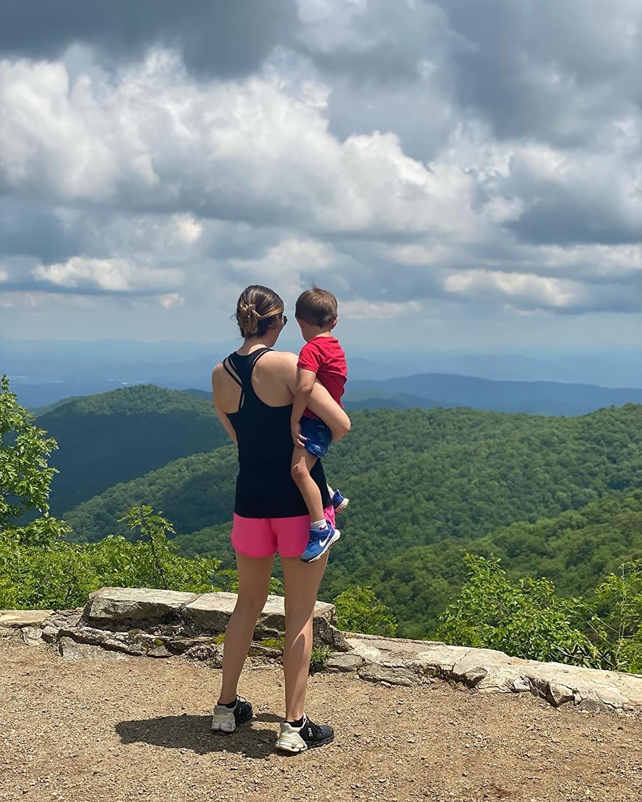 Reviewer standing on mountain lookout in pink shorts holding child at waist
