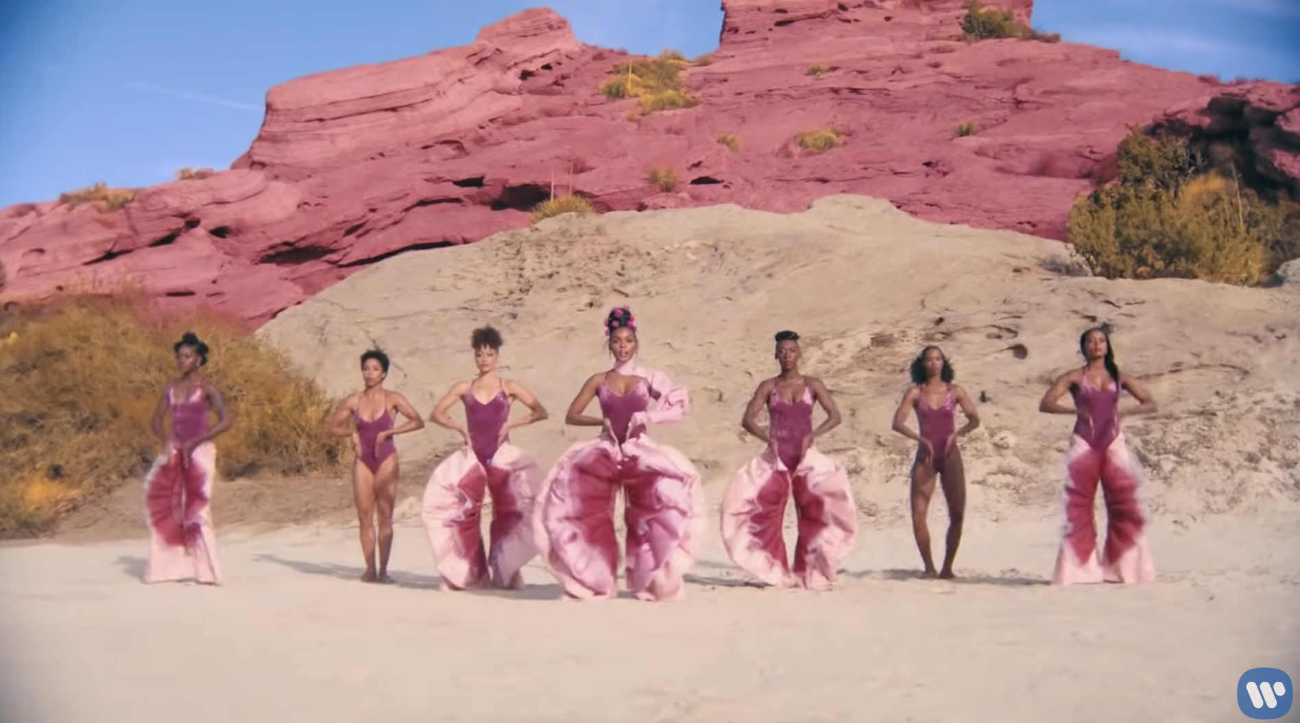 Janelle Monáe and six dancers in the desert, wearing pink bodysuits and frilly pink-and-magenta pants