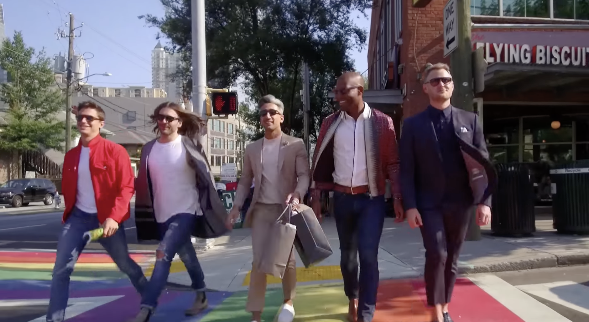 A shot of the five Queer Eye guys walking across a street that is painted with rainbows