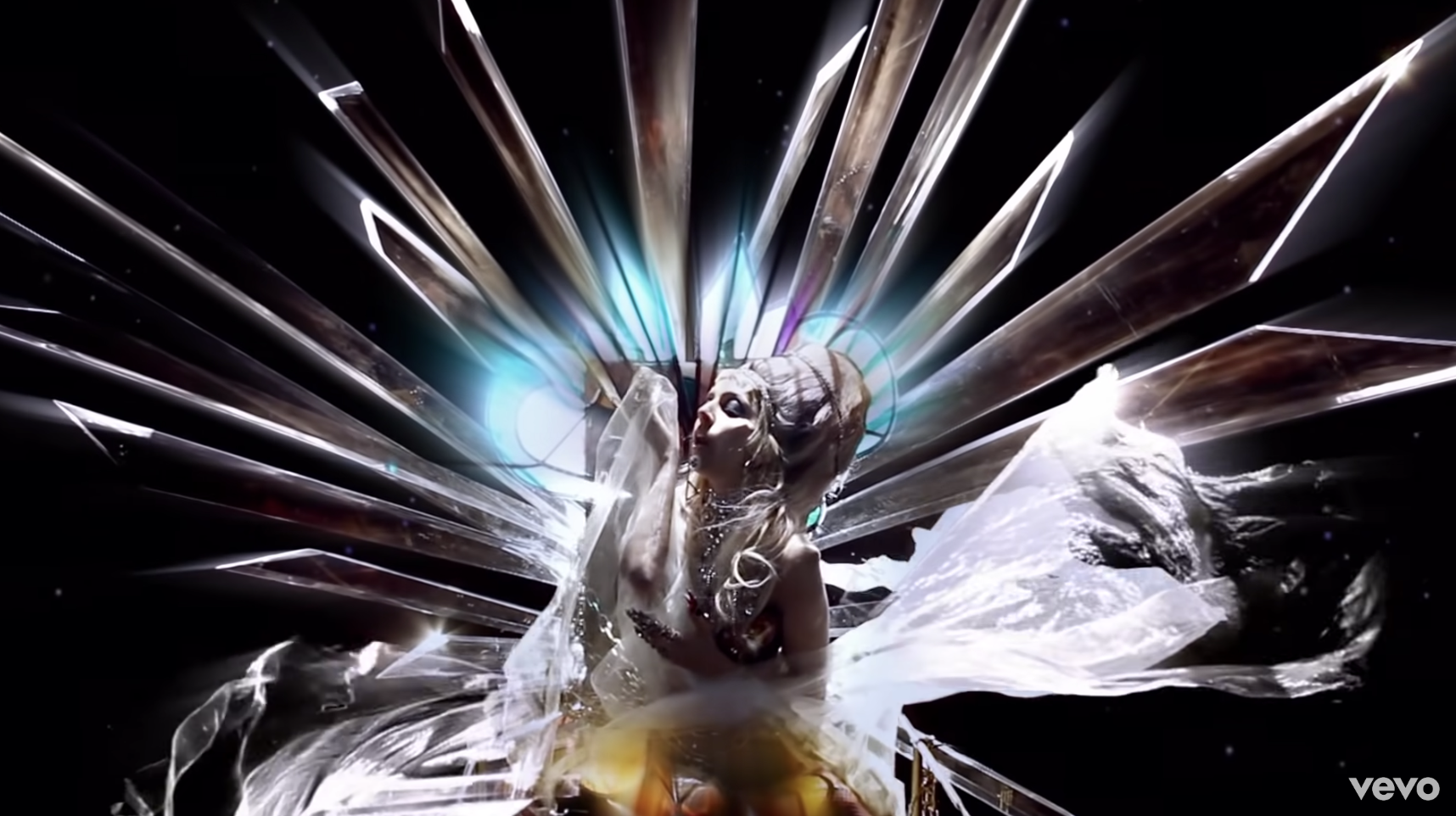 In a screenshot from Lady Gaga&#x27;s music video, she&#x27;s dressed in silver with shiny prism light surrounding her