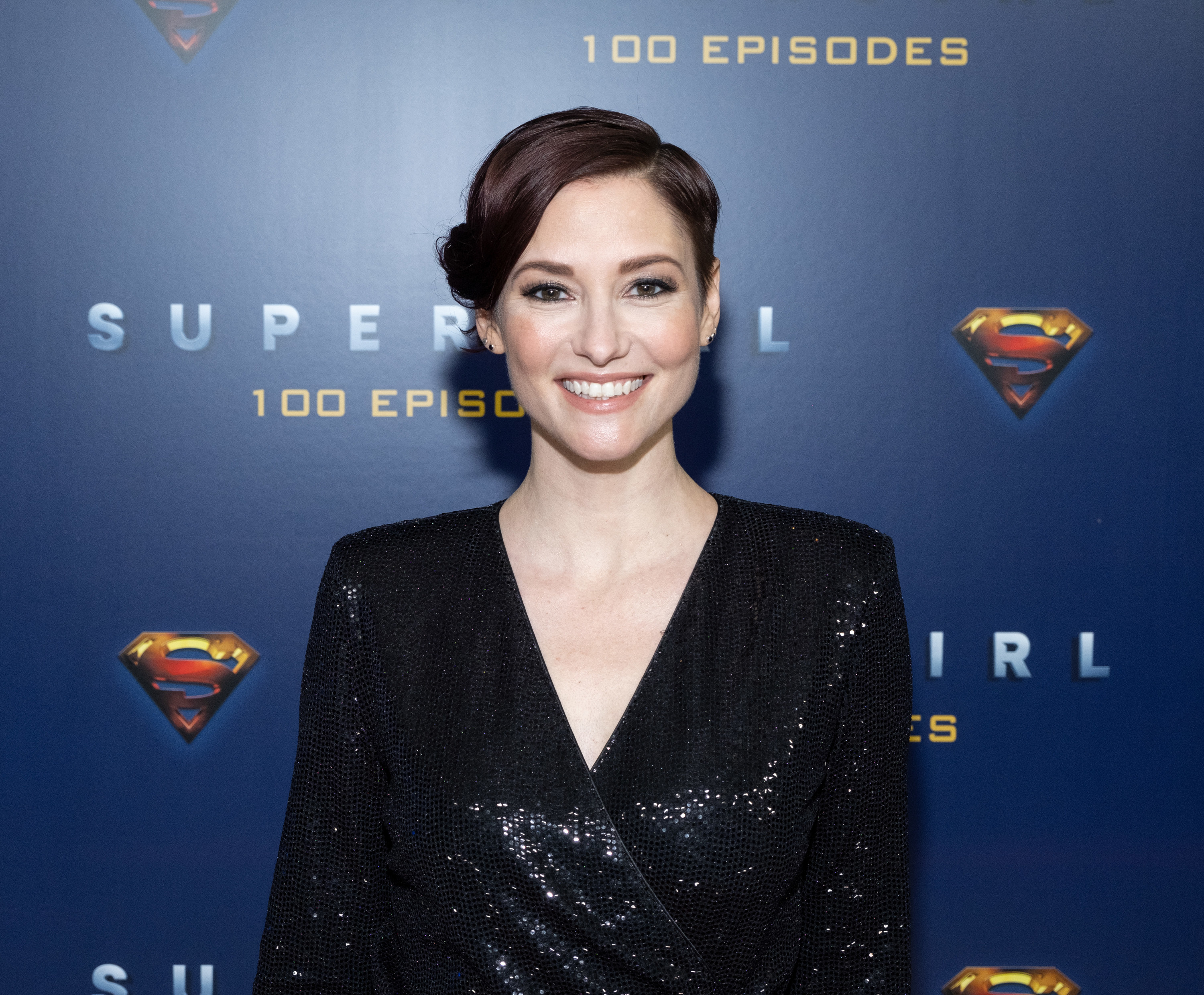 Chyler Leigh poses at a Supergirl event in a shimmery black V-neck dress