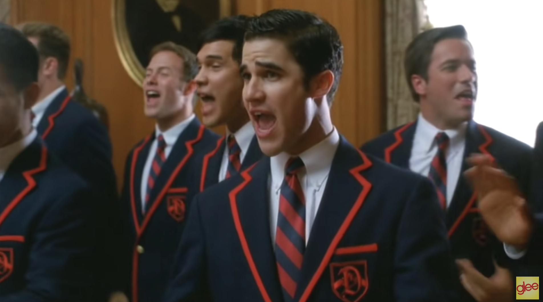 A Glee screenshot, showing Darren Criss wearing a red-and-blue uniform blazer and singing