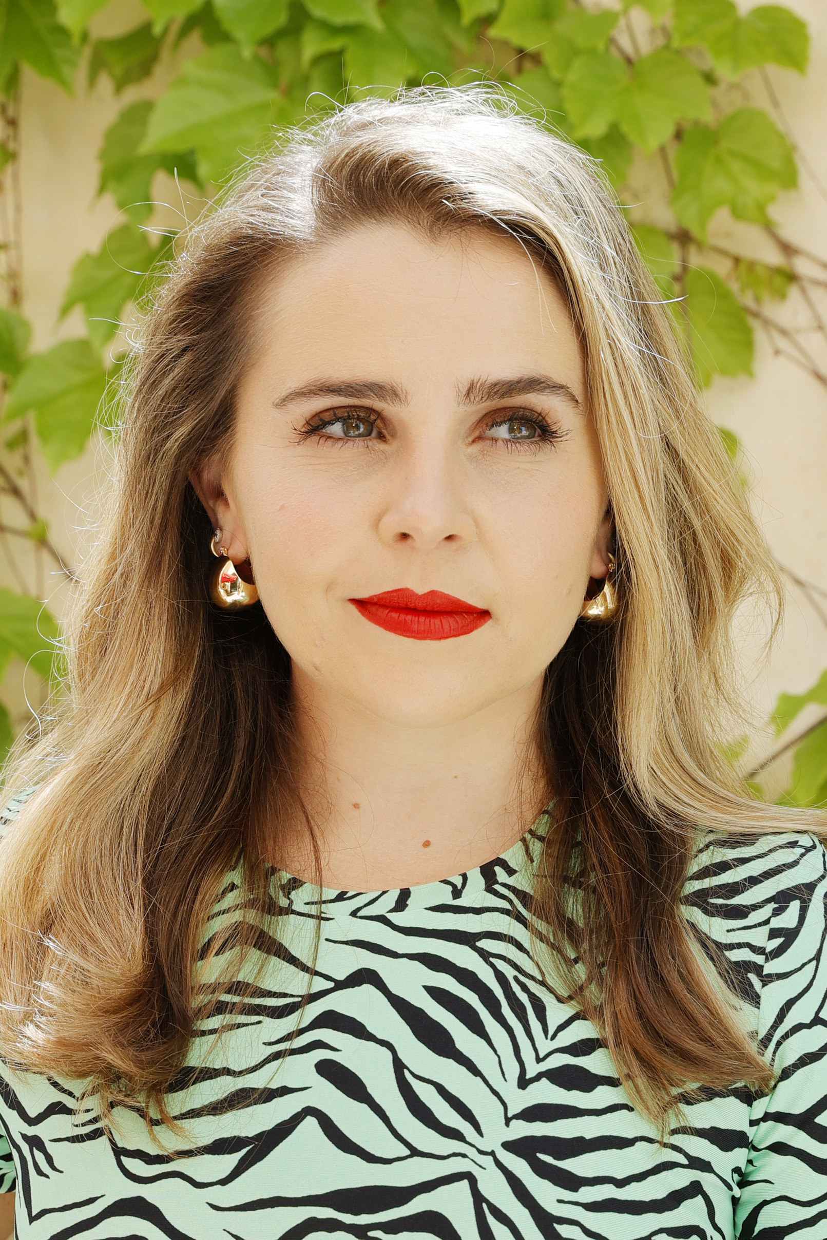 Mae Whitman wearing a mint green zebra print shirt, with red lipstick and gold hoops