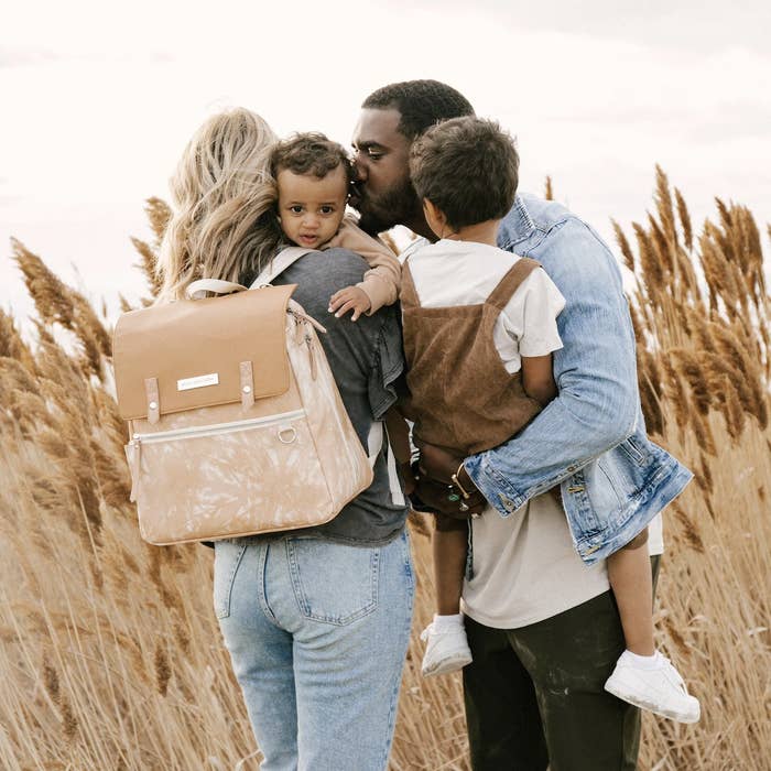 family in field with each parent holding a child and backpack on mother&#x27;s back