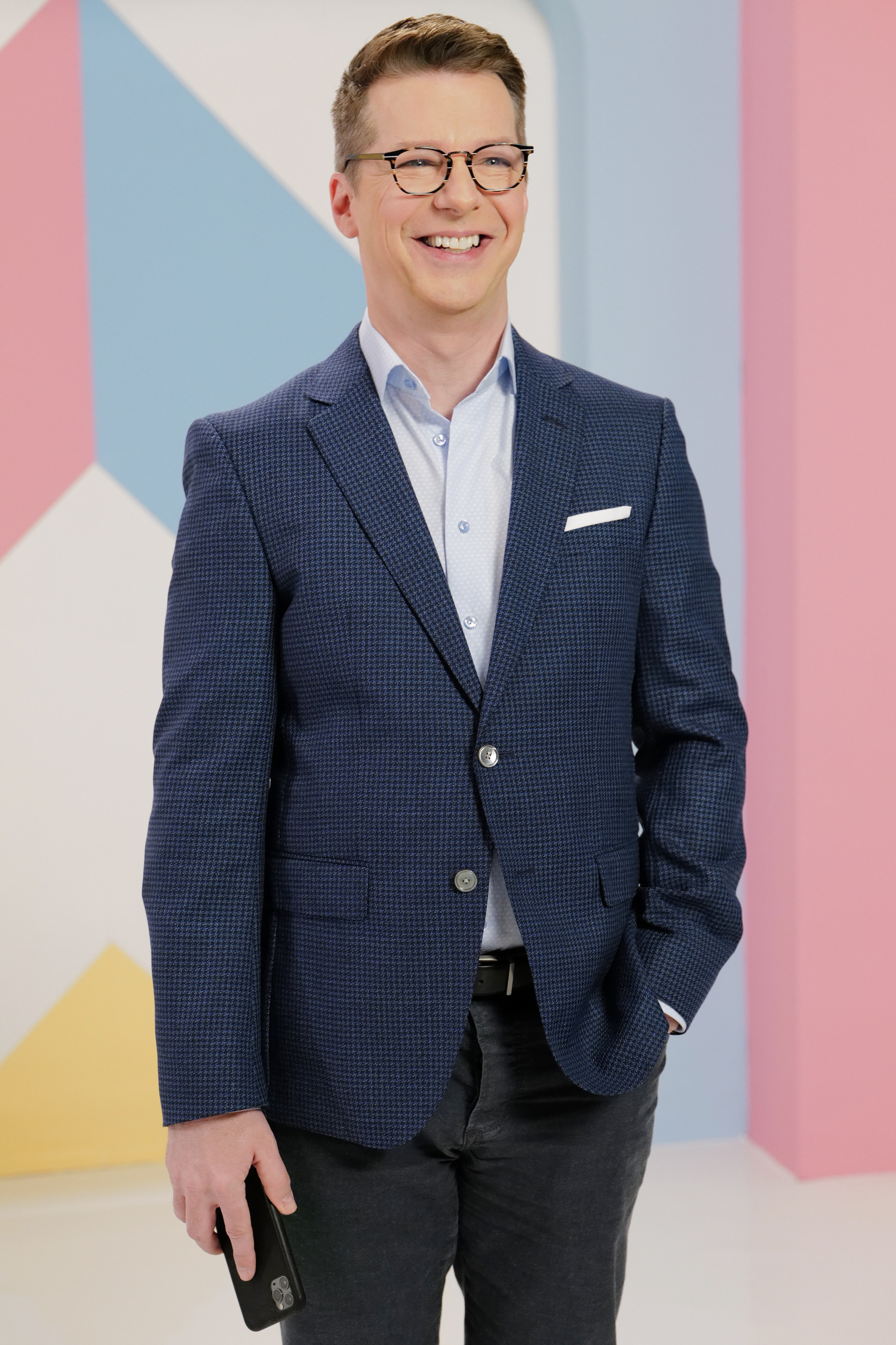 Sean Hayes wears a blue tweed jacket and black jeans while on the set of a TV show
