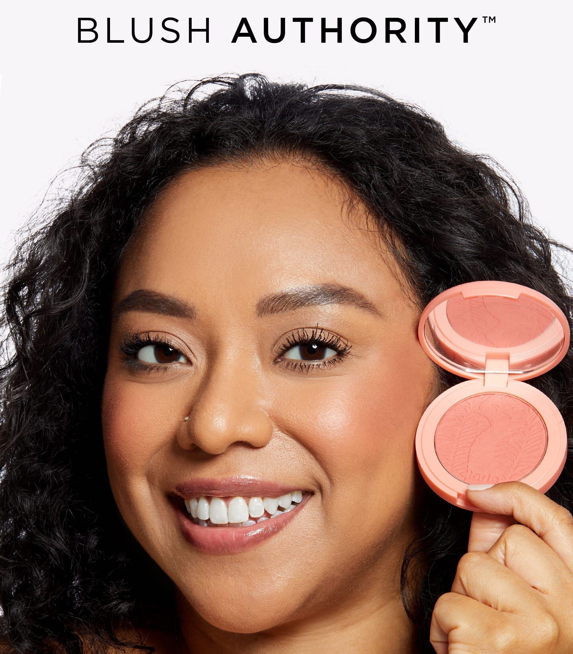 A model holding and wearing a Tarte Blush