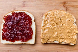 A slice of bread with jelly on it and slice of bread with crunchy peanut butter on it